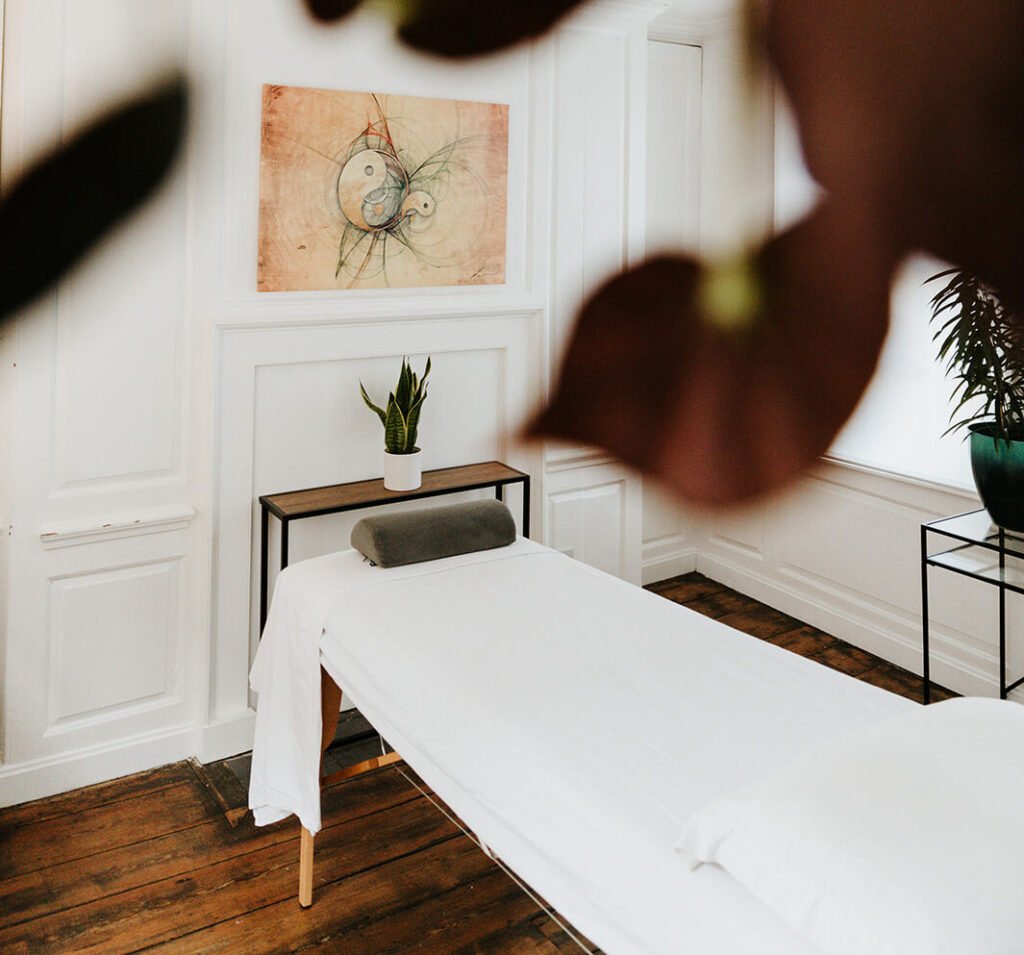 A massage table in a bright treatment room at Soma Wellbeing Centre, seen through foreground leaves